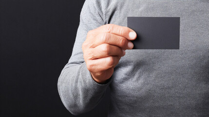 Man hand holds holding blank black business card against dark background. Mockup of rectangular and smooth paper card