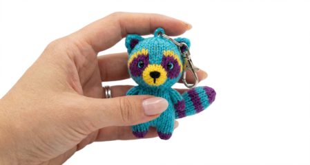 Hand holding a cute knitted raccoon keychain, transparent background
