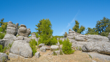 Ancient rock formations and lush greenery of Selge under the bright summer sky.