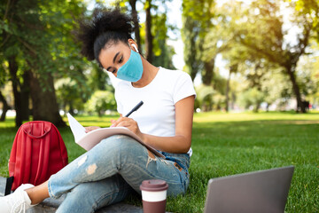 Obraz premium Studentship. African American Student Girl Taking Notes Learning Sitting With Laptop Computer In Beautiful Park Outdoors, Wearing Face Mask. University Education, College Lifestyle And E-Learning