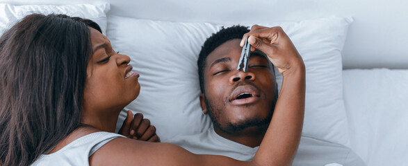 A woman holds a thermometer to a man's forehead while he lies in bed. They appear to be at home in...
