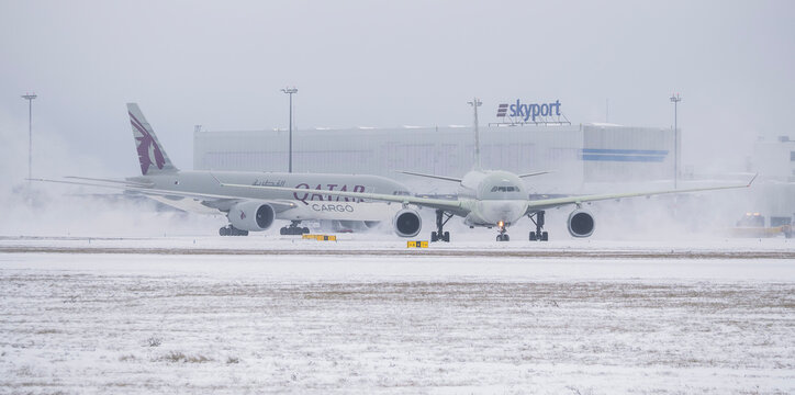 PRAGUE, Czech Republic - January 9, 2026: Qatar Airways Airbus A330 and Qatar Airways Boeing 777-F Cargo aircraft taxiing on the snowy tarmac past the Skyport hangar during a winter storm.