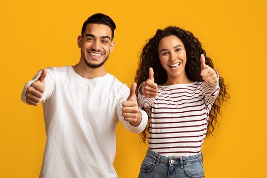 Best Choice. Portrait of happy middle eastern couple gesturing thumbs up at camera, cheerful arab man and woman showing sign of approvel while standing isolated over yellow background, copy space