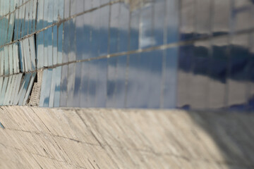 closeup blue tile wall texture damaged grout, cracked ceramic panels reflecting soft sky, urban...