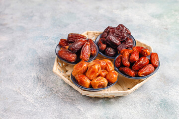 Different types of dates in small blue bowls placed on wicker tray over rustic stone background showcasing variety of dried fruits for ramadan holiday