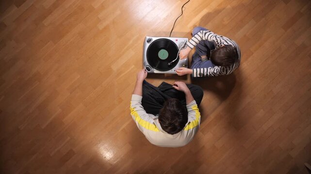 Father and son sit on a wooden floor listening to a vinyl turntable, sharing a retro music hobby, bonding over records and enjoying cozy, multigenerational family time
