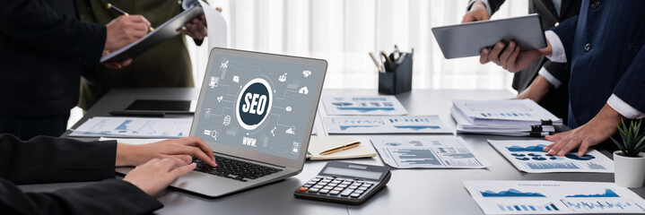 Panorama shot analyst team utilizing BI Fintech to analyze financial report with laptop. Businesspeople analyzing BI data dashboard displayed on laptop screen for business insight. Prodigy