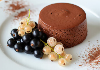 chocolate mousse dessert on a plate with garnish of black and white currant, white currant covered with sugar, cocoa powder used for decoration