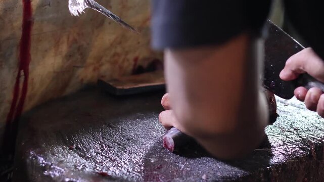 Close up of a fishmonger's hands using a large cleaver to cut fresh tuna on a wooden block at a traditional wet market, capturing authentic local food industry and commerce.