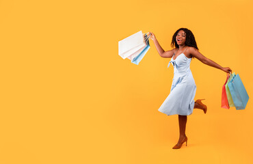 Big sales concept. Full length of young happy black woman running with colorful shopping bags over...