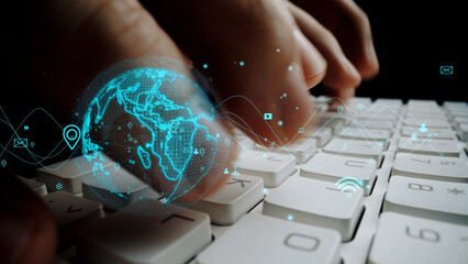A close-up view of hands typing on a keyboard, enhanced with a glowing digital globe overlay, symbolizing global connectivity and the influence of technology in everyday life. Xenic