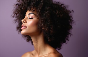 Young african american woman with rich curly hair enjoys a moment of peace with eyes closed and subtle smile. Soft makeup enhances her radiant skin, with a lilac background.