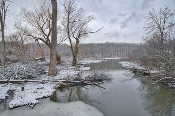 Amid a snow-covered landscape, a small stream flows into a lake in the forest at Wehr Nature Center in Franklin, Wisconsin.