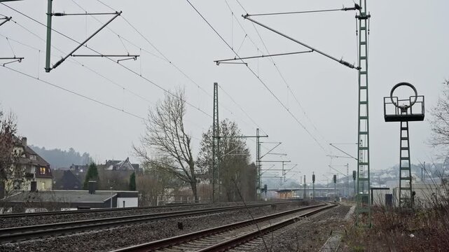 Quiet Train Corridor, Desolate Rural Track Scene, Overcast Countryside Railway With Signals And Distant Horizon, Gray Sky Over Silent Rural Train Tracks With Power Lines And Leafless Trees