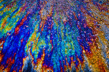 a photograph of an oil or petrol stain on a wet asphalt or pavement surface, a phenomenon called iridescence. interference of light waves reflecting off the different layers of the thin oil film