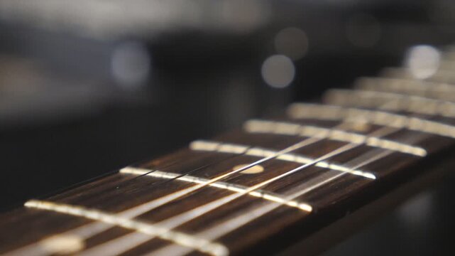 Dolly shot of chords being strummed and vibrating during playing. Close up of trembling guitar strings against fret. Beautiful background with wooden texture. Music performance. Slow motion