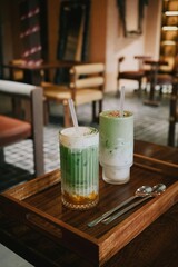 Two matcha latte drinks served on wooden tray in cozy cafe interior. Stylish presentation, natural light, minimal composition. Concept of coffee shop, lifestyle, breakfast, healthy beverage and modern