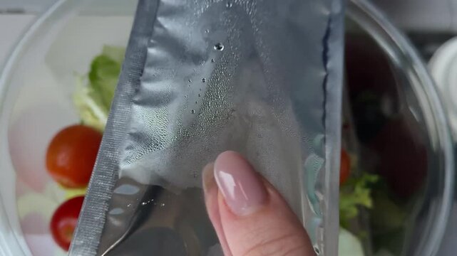 tearing apart a foil packet of salad dressing for home delivery of Caesar salad