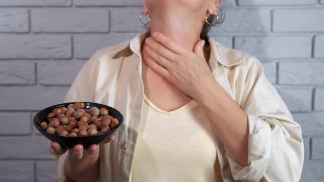 Woman with hazelnut allergy experiencing anaphylactic shock. Woman holding a bowl of hazelnuts and touching her red, swollen neck, showing symptoms of a severe food allergy