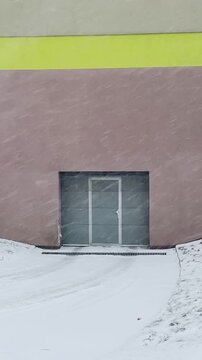 Vertical video of snow covered facade with closed door, metal rollup entrance halfburied in windblown Taken on mobile device.