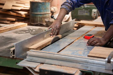 african american Carpenter Cutting Wood Plank with electric table Saw in a woodworking workshop