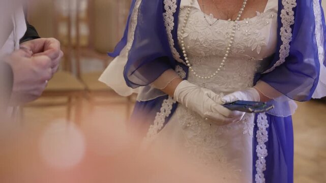 Noblewoman in a beautiful historical gown with white gloves and a pearl necklace standing in a ballroom and holding a blue fan
