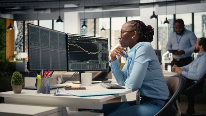 Forex expert in office looking over candlestick charts on screen to assess stock market volatility. African american woman in hedge fund company reading investment reports