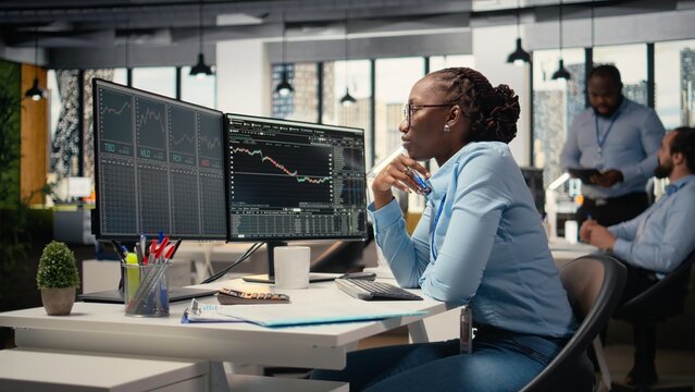 Forex expert in office looking over candlestick charts on screen to assess stock market volatility. African american woman in hedge fund company reading investment reports