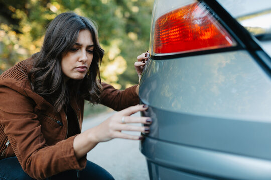Frustrated young woman looking at scratch on her car