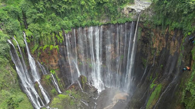 Drone aerial view of Tumpak Sewu Waterfall, East Java, Indonesia. Spectacular dramatic canyon, lush tropical rainforest jungle and majestic volcanic landscape scenery. Famous tourist travel destinatio