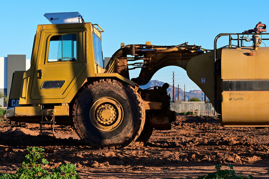 Large scraper vehicle shaping soil on an undeveloped site, representing land grading activity, earthwork processes, and early stage infrastructure development