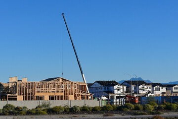 Crane lifting roof trusses at a residential construction site with multiple homes in progress, representing housing development, structural assembly, and suburban building operations