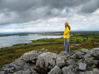 Female tourist in yellow jacket standing in a mountains with stunning view on the ocean and blue...