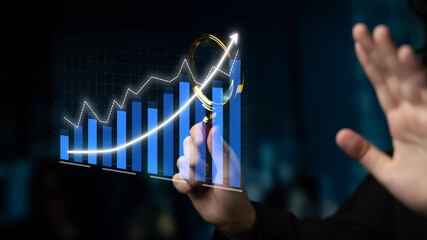 Close-up view of a professional hand examining a digital graph with a magnifying glass, symbolizing growth and analysis in business and market trends. Impute