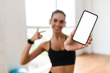 Fitness Application. Smiling slim young woman in sportswear holding mobile phone and pointing at...