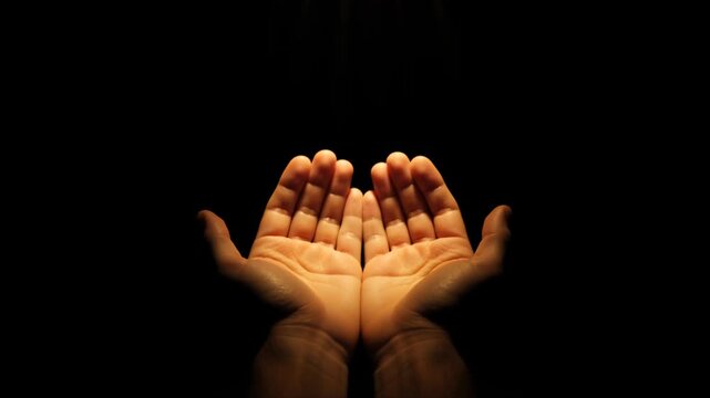 Close-up of open hands cupped together in a spotlight against a black background. Gesture of prayer, begging, or receiving charity. Hope and spirituality concept