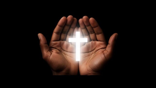 Cupped black hands holding a glowing Christian cross against a black background. Spiritual concept of faith, prayer, and divine light