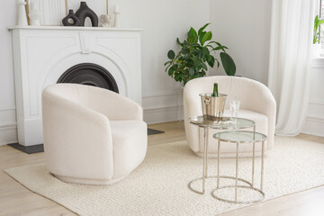 Minimalist living room with soft white armchairs, glass coffee table with ice bucket and glasses and elegant decor, creating cozy and stylish interior atmosphere with natural daylight.
