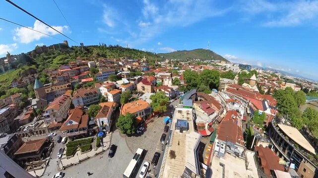 Ascending in a cable car, revealing a stunning panorama of Tbilisi, Georgia's capital, with the Kura River, historic architecture, and lush greenery under a blue sky