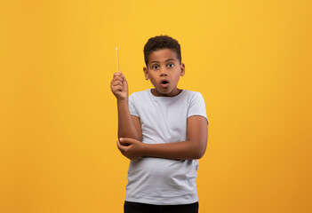 Amazed black boy schooler raising pencil up over yellow studio background, smart kid with shocked...