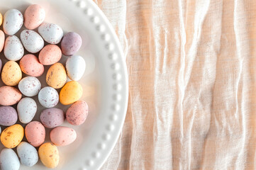 Colorful Easter chocolate eggs in a plate on a beige background, top view with copy space.