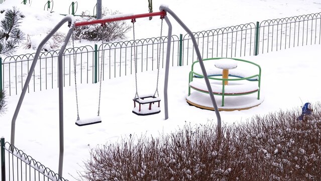 Plac zabaw z huśtawkami i karuzelą pokryty śniegiem