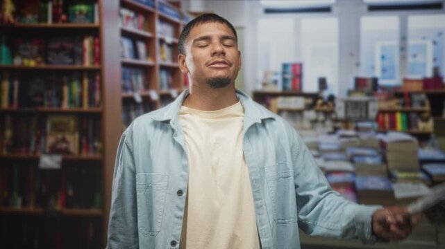 Man stretching arms wide while holding dollars in hand inside a bookstore, smiling with closed eyes and casual jacket; celebration success.