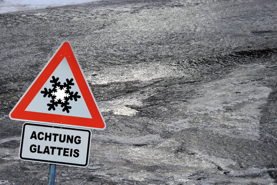 Unfallgefahr und Risiko durch Glatteis. Ein Schild mit Hinweis Achtung Glatteis und eine eisbedeckte Stra&szlig;e 