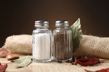 Salt and pepper shakers with spices on wooden table against brown gradient background, closeup