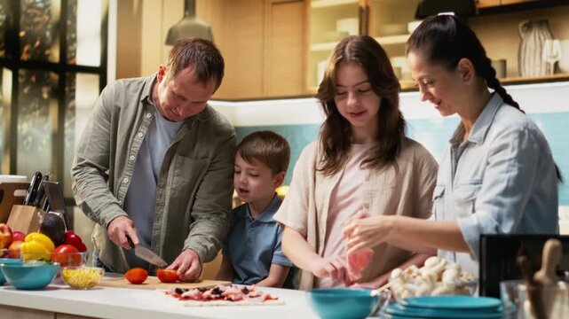 Joyous parents teaching their kids to cook and cut vegetables safely, family enjoys making homemade pizza from old recipe. Mom and dad explaining steps for efficient cooking. Camera B.