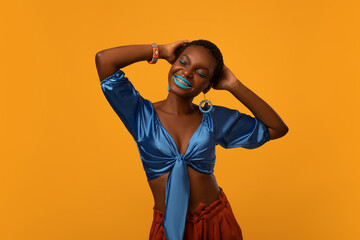 Relaxed african american millennial woman in bright ethnic clothes and breathtaking makeup dancing...