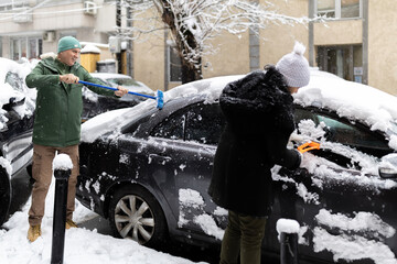 Couple clearing snow from car after winter snowfall
