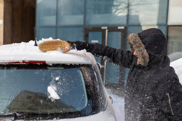 Man clearing snow from car using broom in winter © Jelena