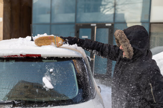 Man clearing snow from car using broom in winter